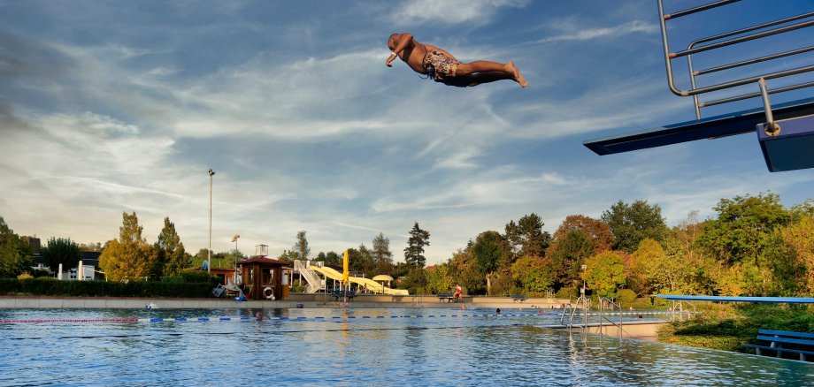 Ein Mann springt im Freibad vom 3 Meter Turm in das Wasser