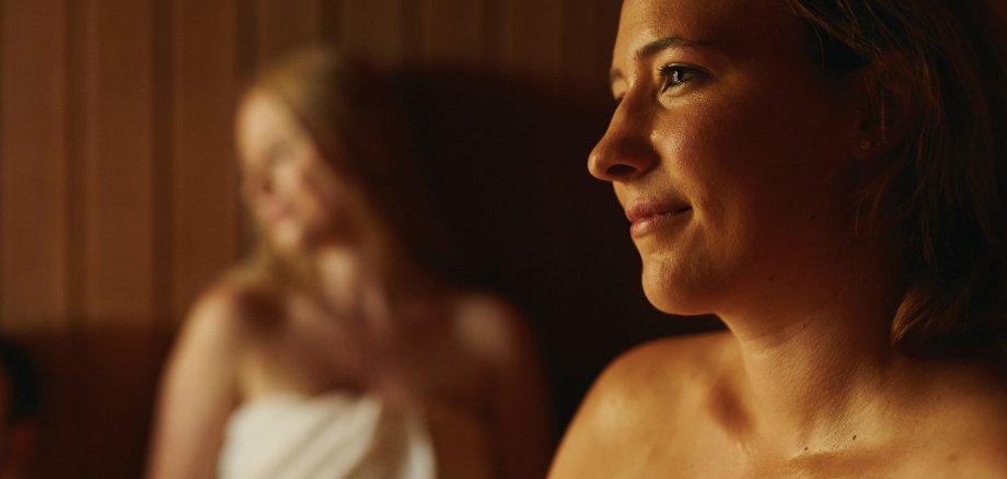 Panoramabad Stromberg Im Fokus eine zufrieden aussehende Frau die sich in der Sauna entspannt und eine weitere Frau im Hintergrund