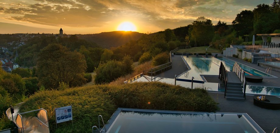 Ein Freibad mit mehreren Becken und einer Wasserrutsche bei Sonnenuntergang