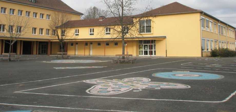 Das gelbe Schulgebäude der Grundschule Langenlonsheim aus Sicht vom Schulhof.