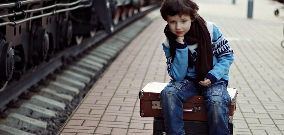 Ein Kind sitzt am Bahngleis und wartet auf seinen Zug.