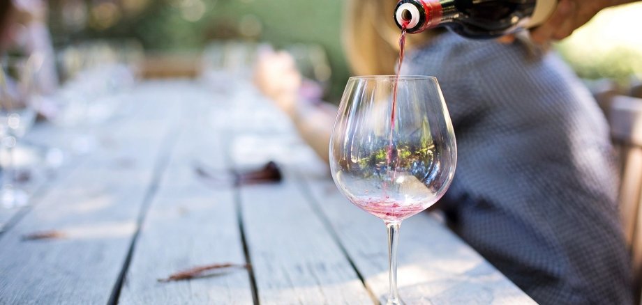 Ein leeres Weinglas, welches draußen auf einem Tisch steht und mit Wein befüllt wird.