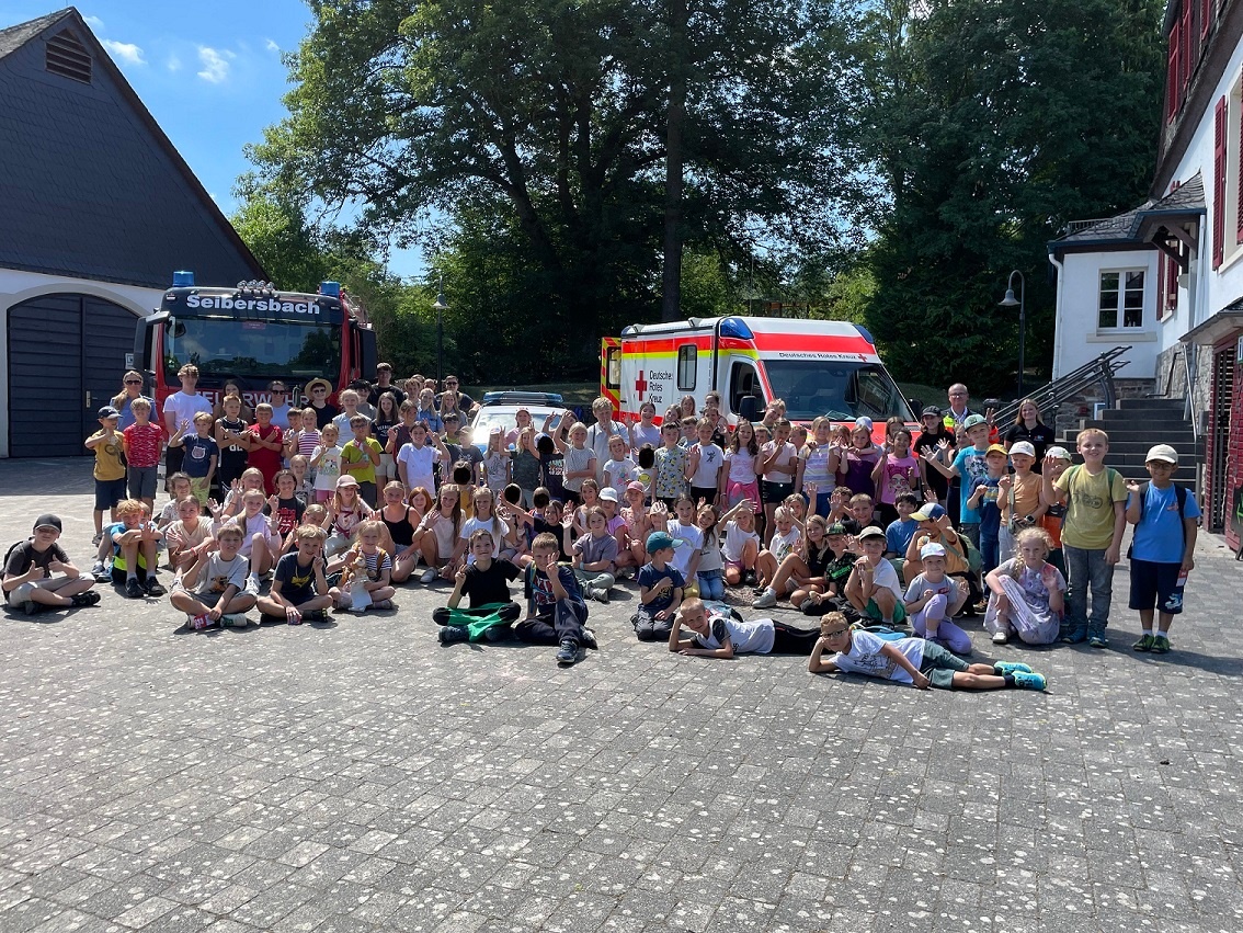 eine große Gruppe von ca. 60 Kindern bei der Ferienfreizeit vor verschiedenen Rettungsfahrzeugen
